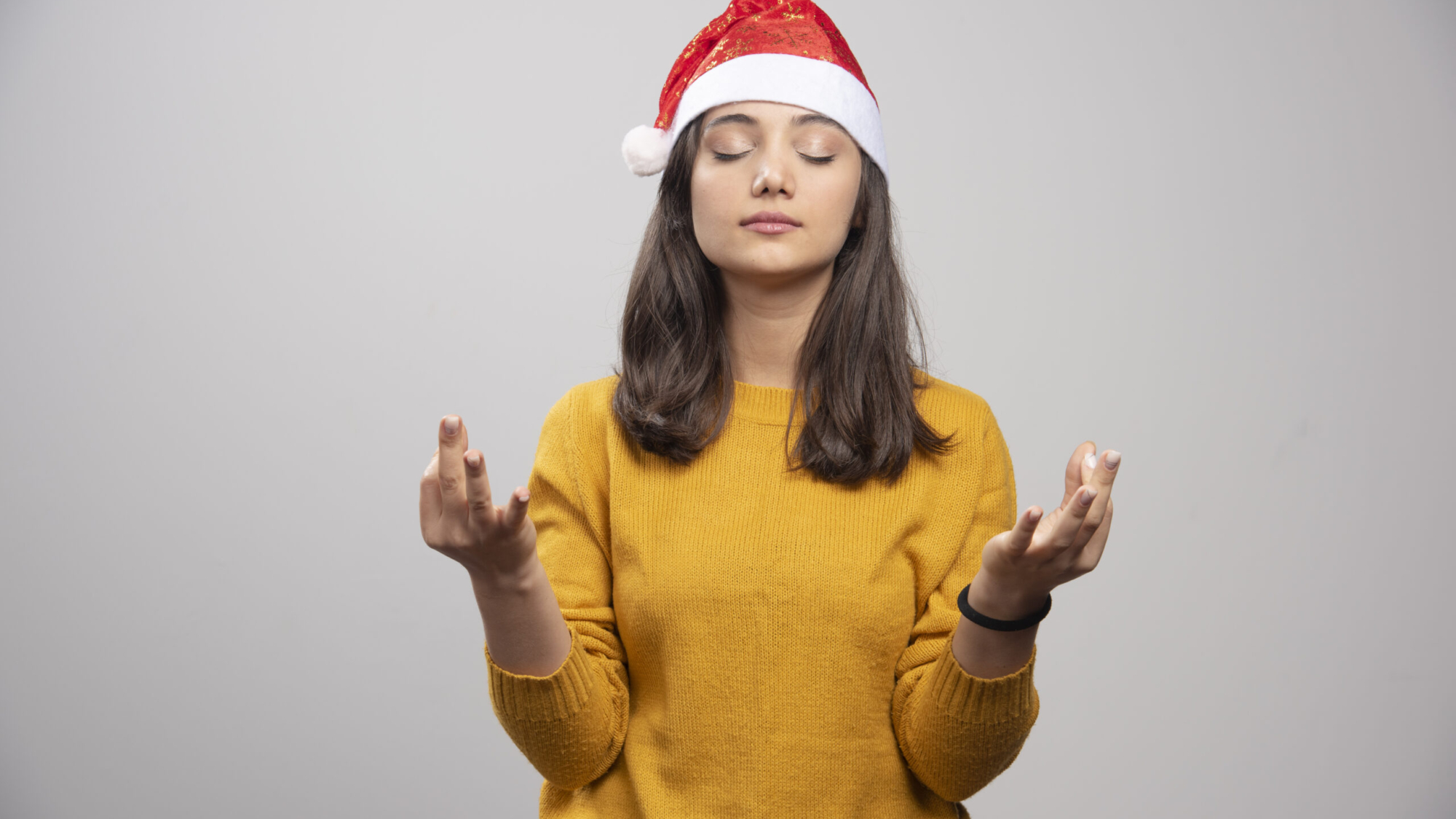 Woman in Santa hat doing meditation on gray background. High quality photo