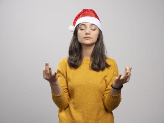 Woman in Santa hat doing meditation on gray background. High quality photo